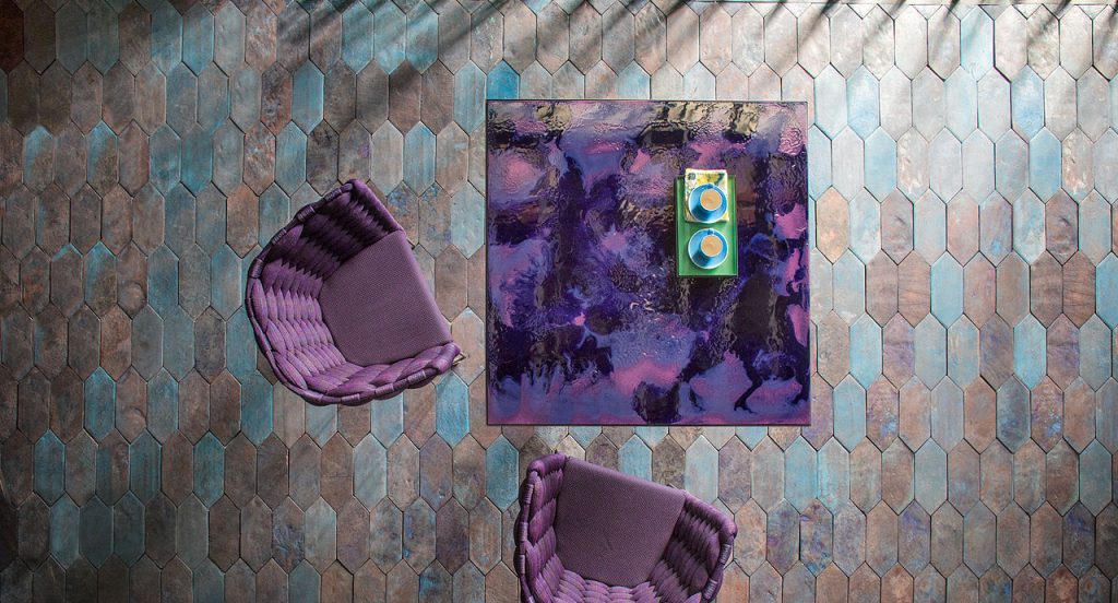 Cafe square table, purple abstract pattern top with black steel central leg with four spokes and two chairs in a dining room.
