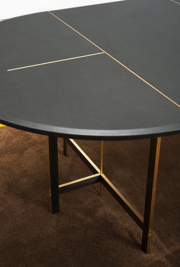 A Placè Dining Table. Base in brass with bronzing oxidation on the flat part and satin finish on the thickness, with wax finish. Leg connection plate in matte black metal. MDF top with reinforcing black leather-covered aluminium sheets. Decorative inserts in satin-finished brass with wax finish.