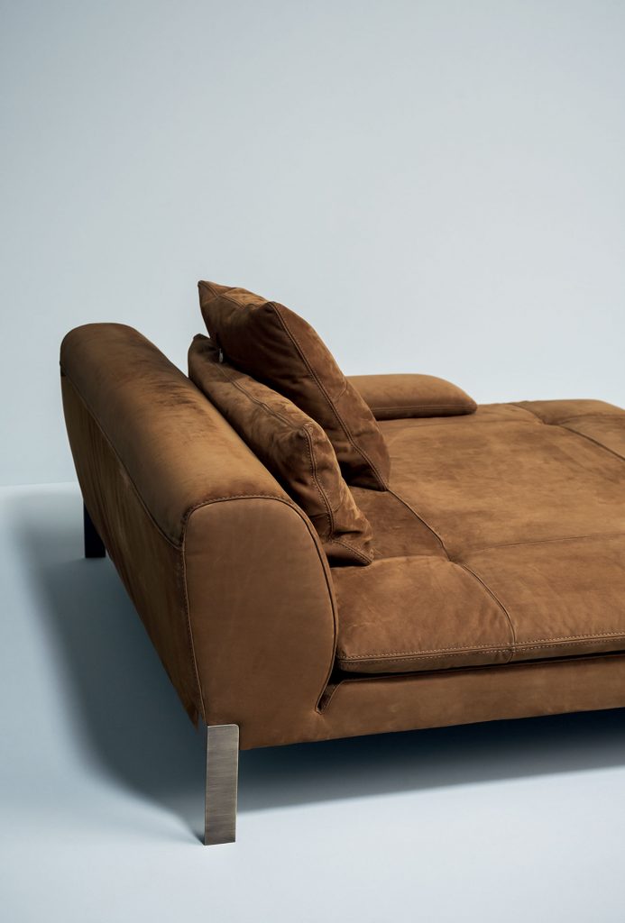A brown Victor sofa module for two with low back. Brassed metal feet and support hook. Covers in leather in a dining room.