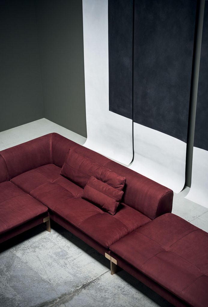A red Victor sofa divided into three modules, two modules for two. One for two with low back. Brassel metal feet and support hook. Covers in leather in a dining room.