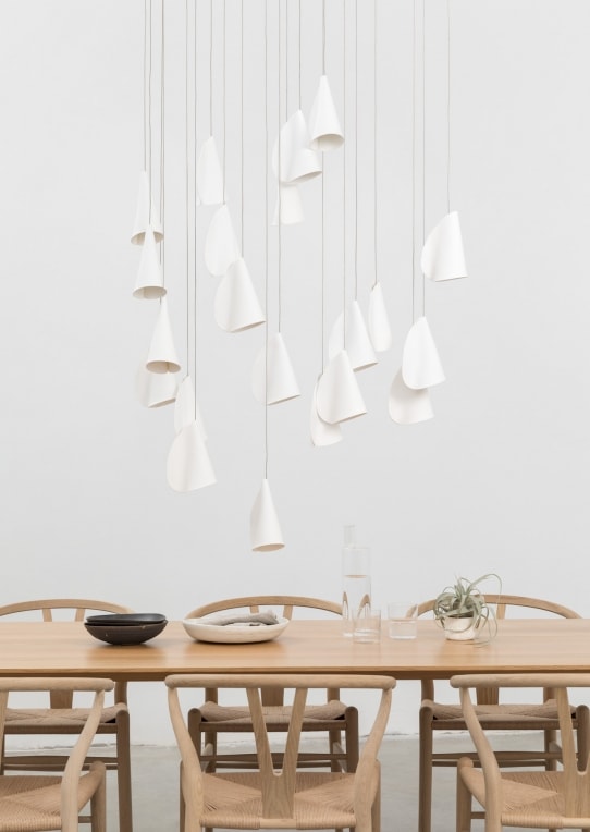 A Twenty One lamp made of porcelain, blown borosilicate glass, braided metal coaxial cable, electrical components, brushed white powder coated canopy in a dining room background.