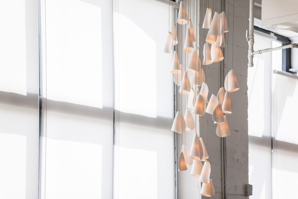 A Twenty One lamp made of porcelain, blown borosilicate glass, braided metal coaxial cable, electrical components, brushed white powder coated canopy on a white room background.