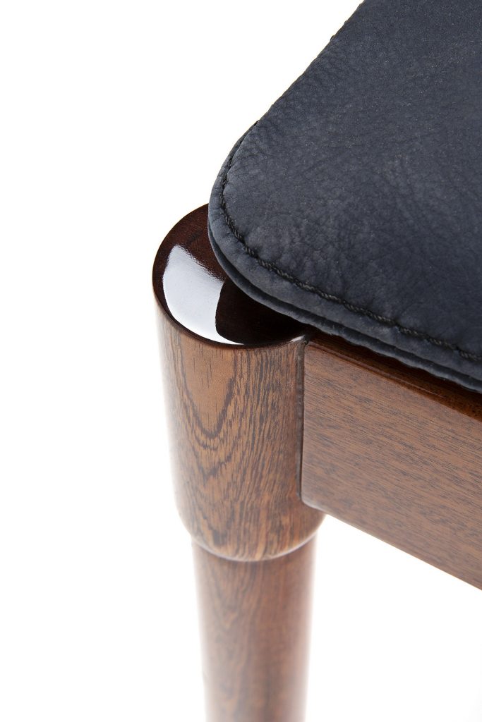 Closeup of Vieste Pouf: Rectangular pouf with a black cushioned top and four brown legs on a white background.