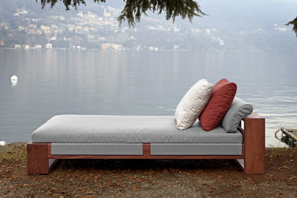 Bellagio Chaise Longue: Beige chaise longue with cushioned seating and wooden legs next to a lake.