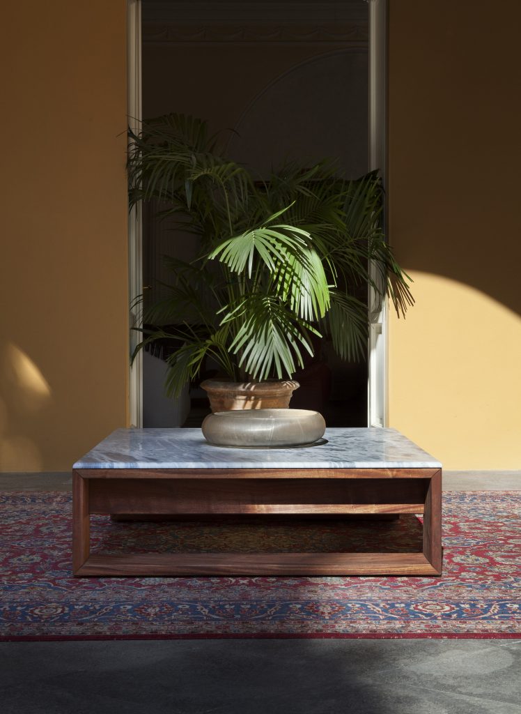 Bellagio Coffee Table: Rectangular top in white and gray marble with a brown base in a hallway.