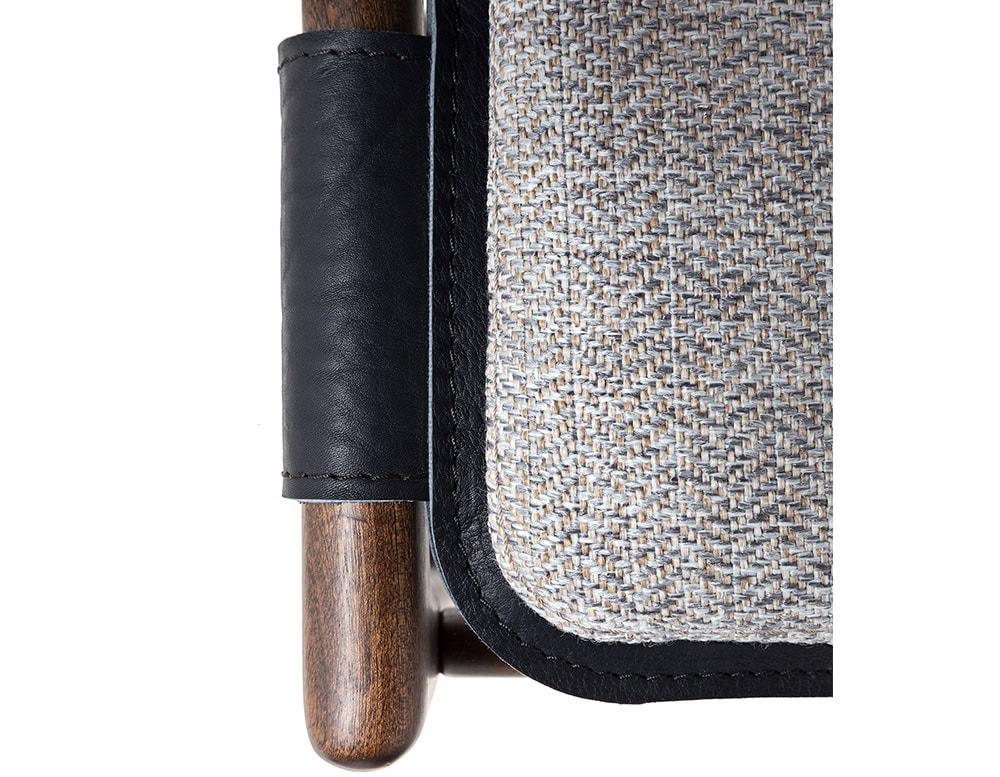 Closeup of Levante Chair. Structure in brown wood, seat and backrest in black leather with gray cushions on a white backrground.
