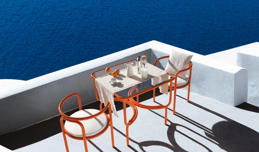 locus solus dining table in orange with two orange chairs with an ocean view
