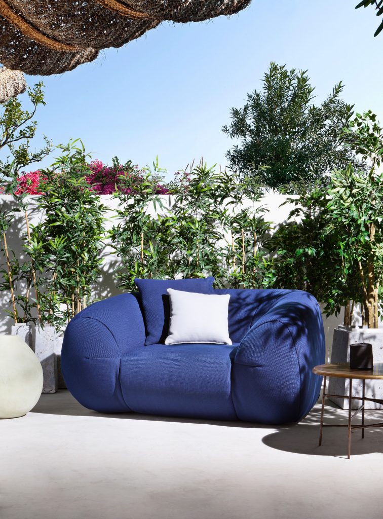 palau armchair in blue with a white pillow on top surrounded by plants