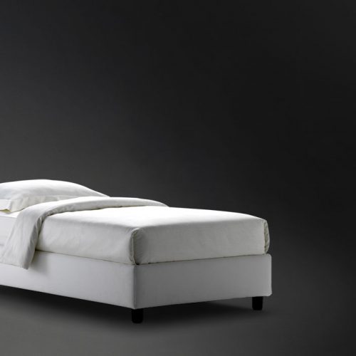 Sommier Single bed. White base with four black wheels and a mattress on a black background.