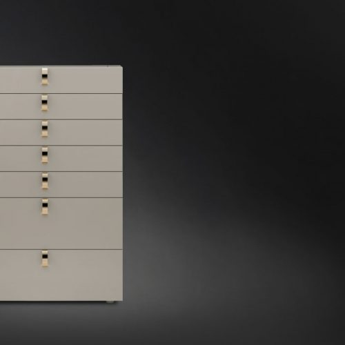 Tallboy Splendor. White structure with seven drawers with seven golden handles on a black background.