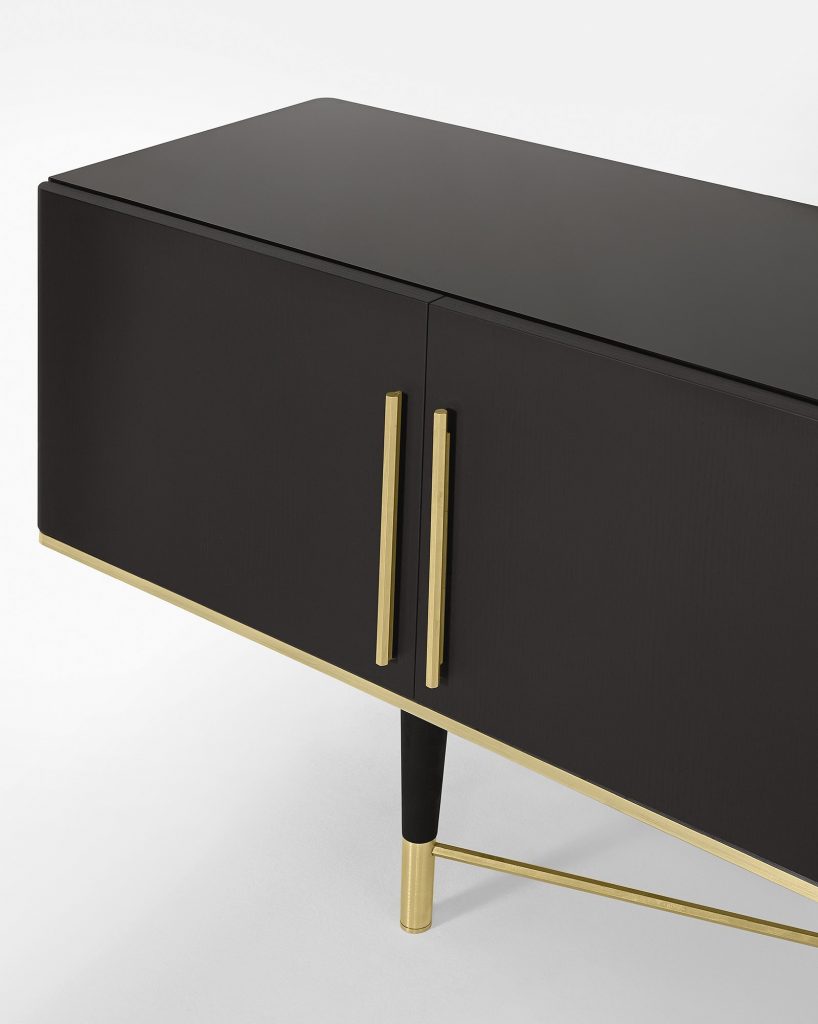 Closeup of Tama Crédence: A black wooden console table with storage compartments and gold legs on a white background.