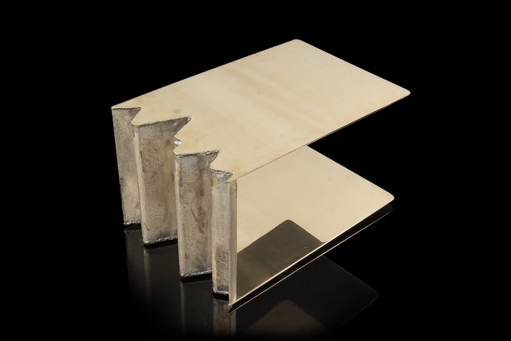 Be Mine side table. Base and top finish in brass with pointed edge on a black background.