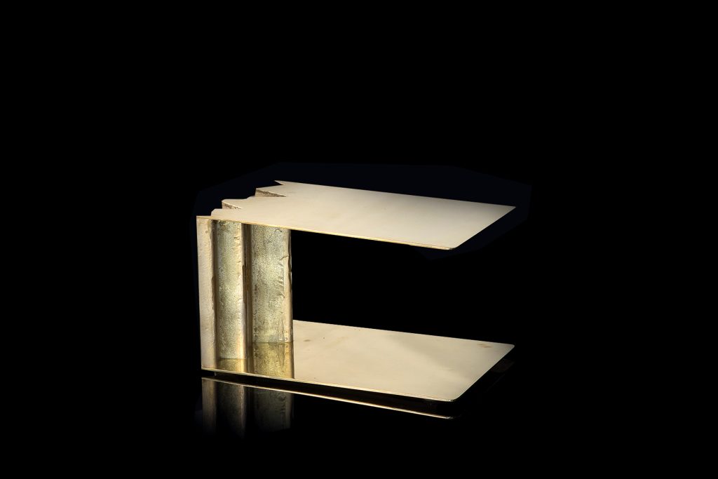 Be Mine side table. Base and top finish in brass with pointed edge on a black background.