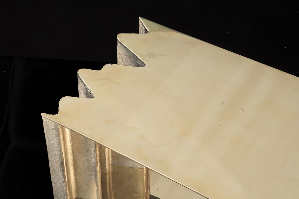 Closeup of Be Mine side table. Base and top finish in brass with pointed edge on a black background.