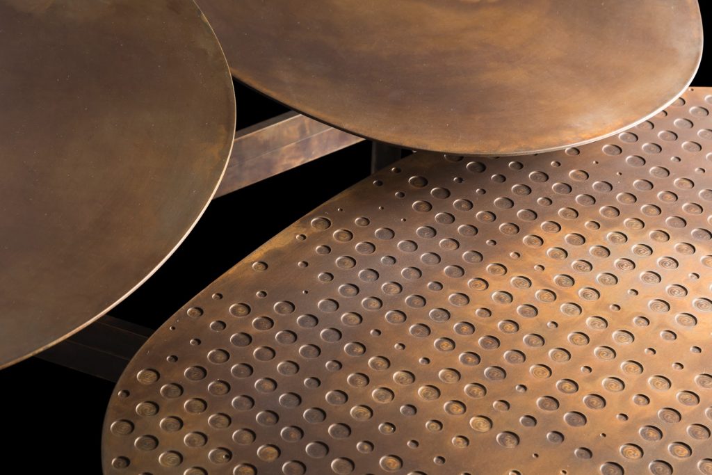 Coseup of Galaxy table with three round giratory tables made of metal and brass on a black background.
