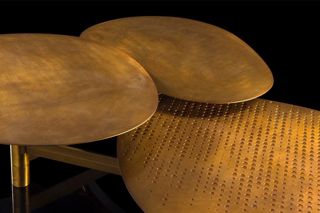Coseup of Galaxy table with three round giratory tables made of metal and brass on a black background.