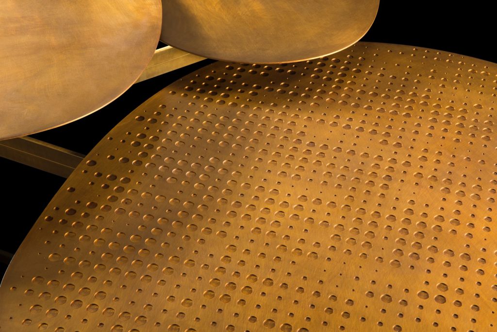 Coseup of Galaxy table with three round giratory tables made of metal and brass on a black background.