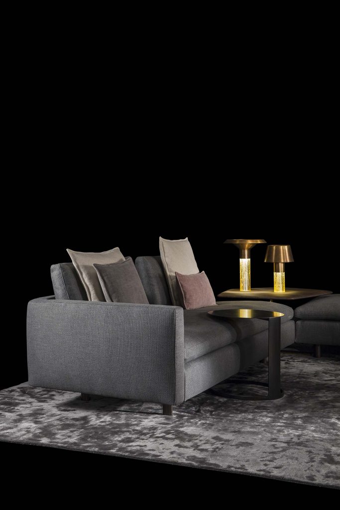 Human Sofa with armrest and backrest upholstered in gray fabric with black brass legs in a living room.