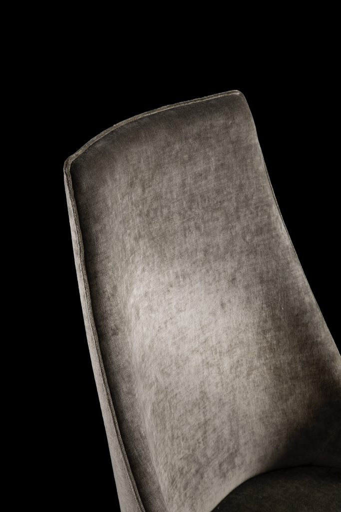 Closeup of Is A Chair in gray fabric on a black background.