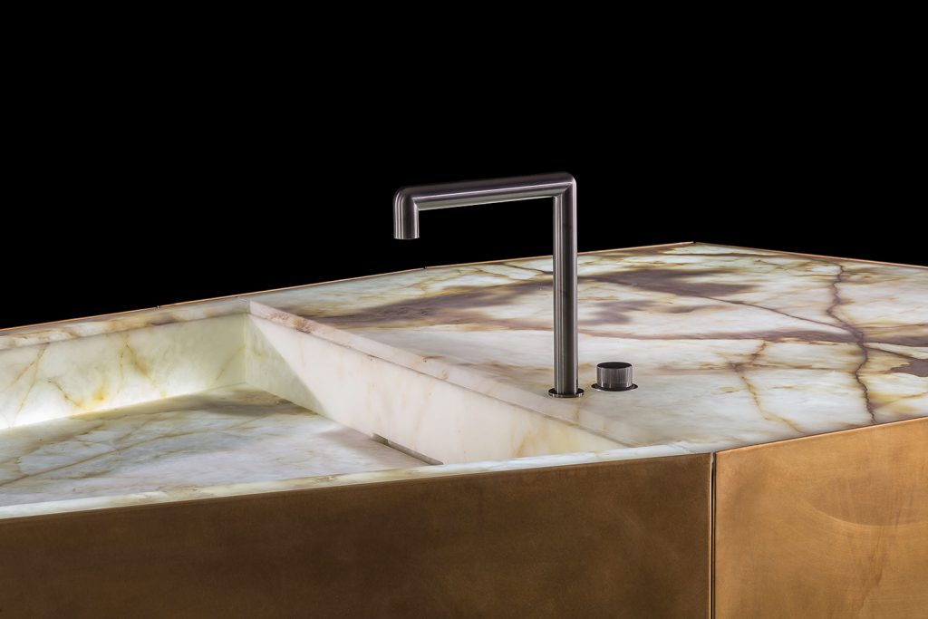 Ozone Evo kitchen bar, cover in brass, top and sink in white and brown irregluar pattern marble stone with black faucet on a black background.