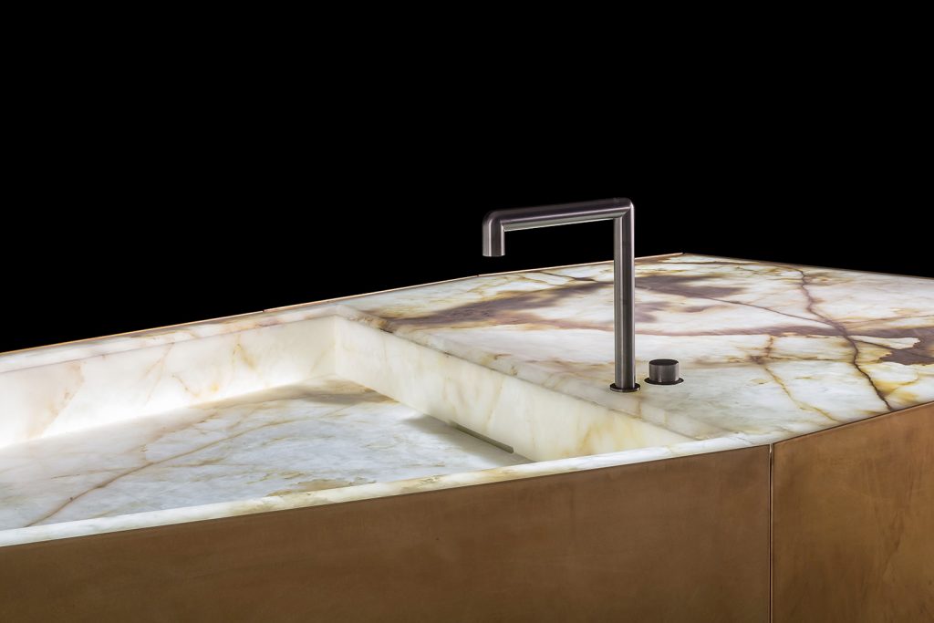 Ozone Evo kitchen bar, cover in brass, top and sink in white and brown irregluar pattern marble stone with black faucet on a black background.