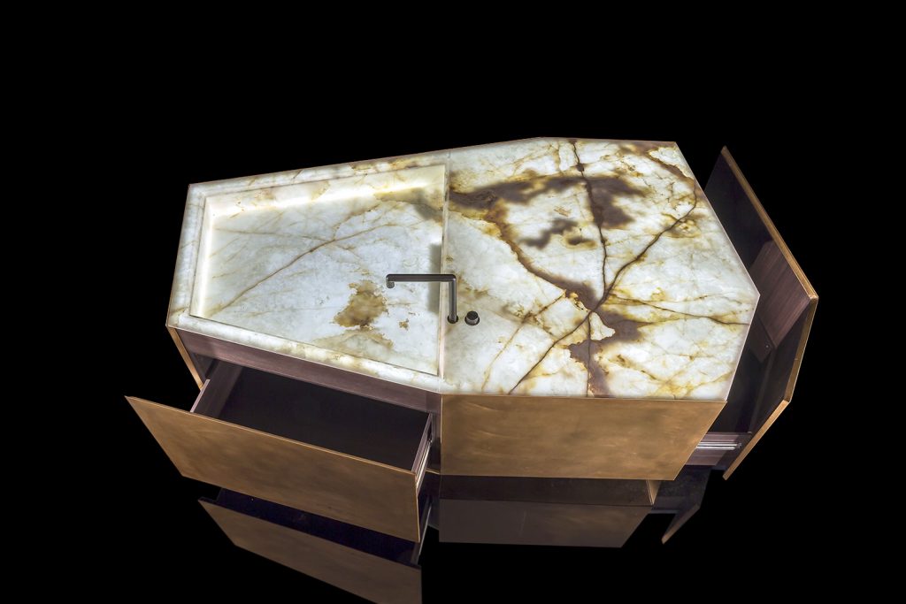 Ozone Evo kitchen bar and drawer cover in brass, top and sink in white and brown irregluar pattern marble stone with black faucet and on a black background.