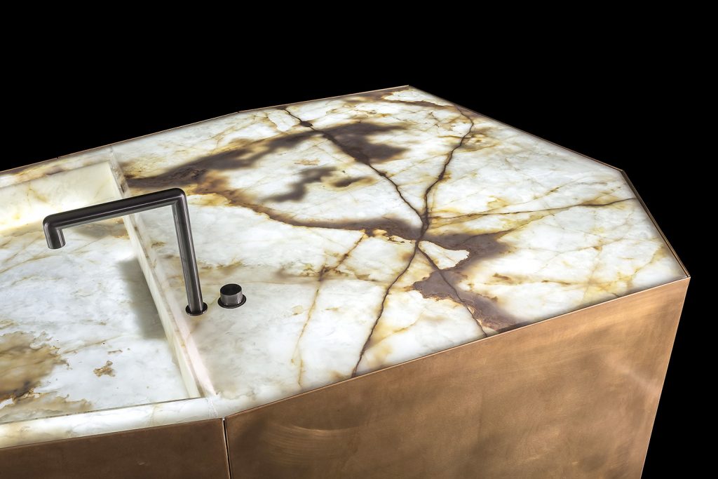 Ozone Evo kitchen bar, cover in brass, top and sink in white and brown irregluar pattern marble stone with black faucet on a black background.