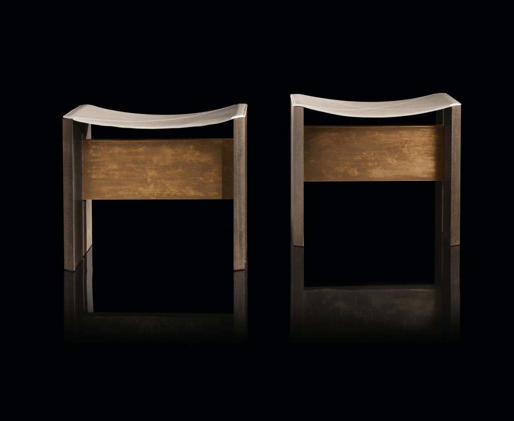Two Rio Stools, structure and two legs in natural wood with central crosspiece covered in brass; seat in gray leather on a black background.