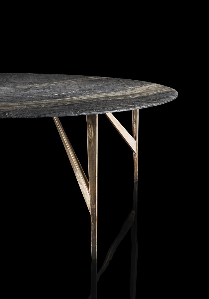 Round Saetta Table, four legs in sandlasting brass and bronze. Top in gray and black stone on a black background.