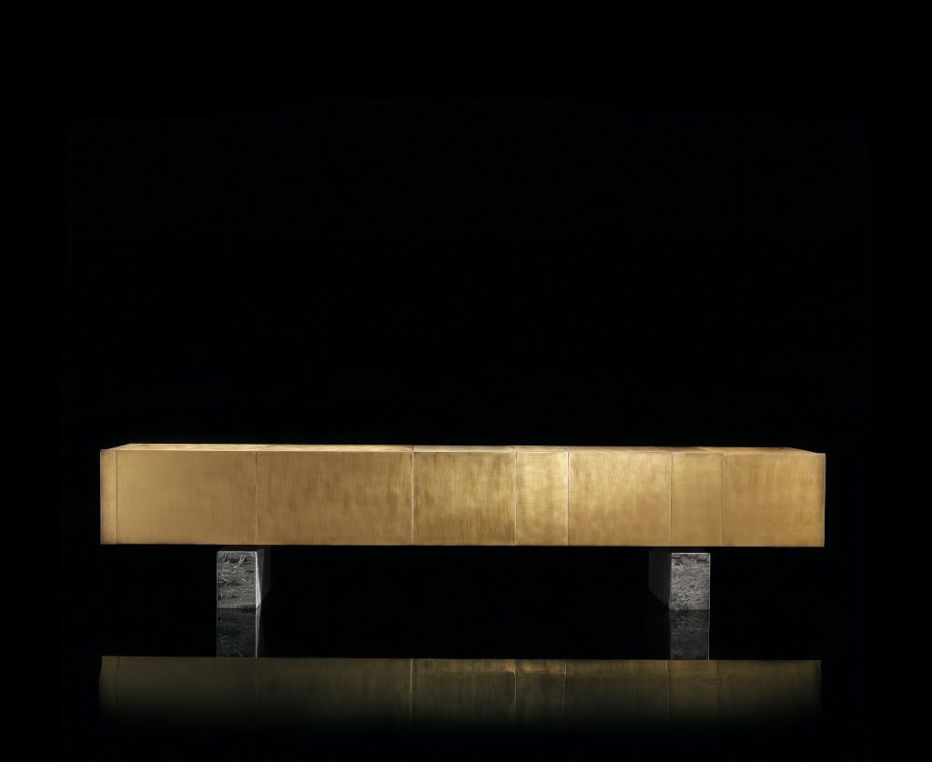 Slim Side sideboard. Structure and two doors finish in brass. Two legs in gray and black stone on a black background.