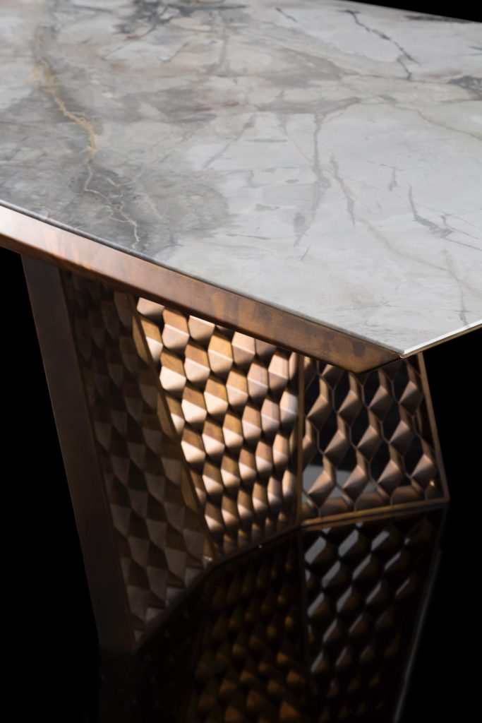 Closeup of stealth Table, legs in brass finish with rhombus pattern, top in white and gray marble stone on a black background.