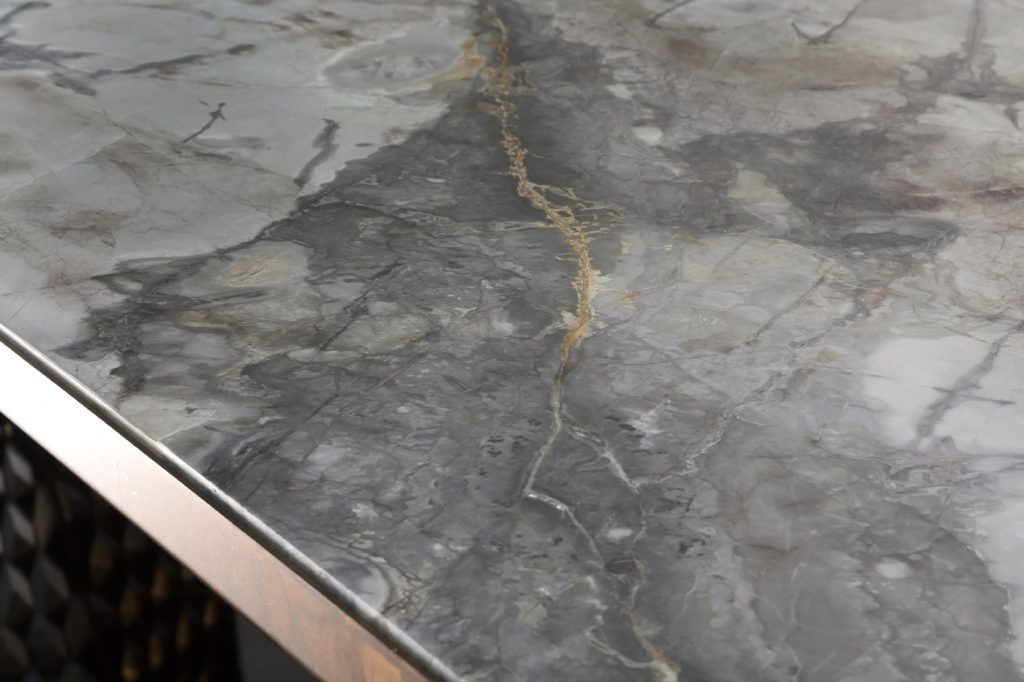 Closeup of stealth Table, legs in brass finish with rhombus pattern, top in white and gray marble stone on a black background.