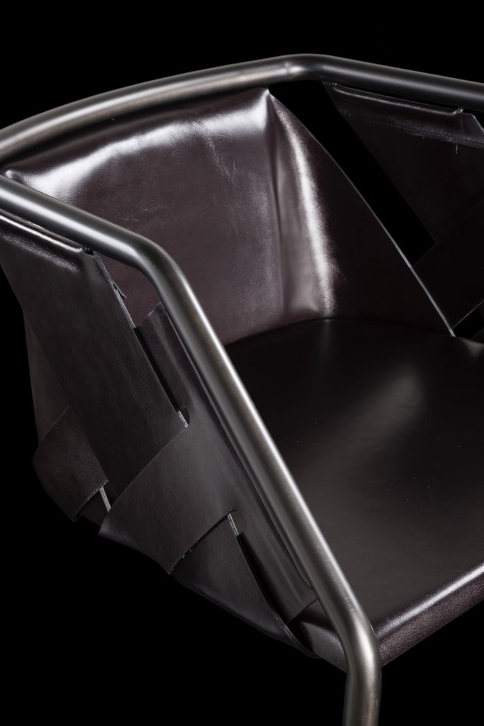 Closeup of Strip Stool. Structure in curved black metal frame, seat covered with brown leather on a black background.