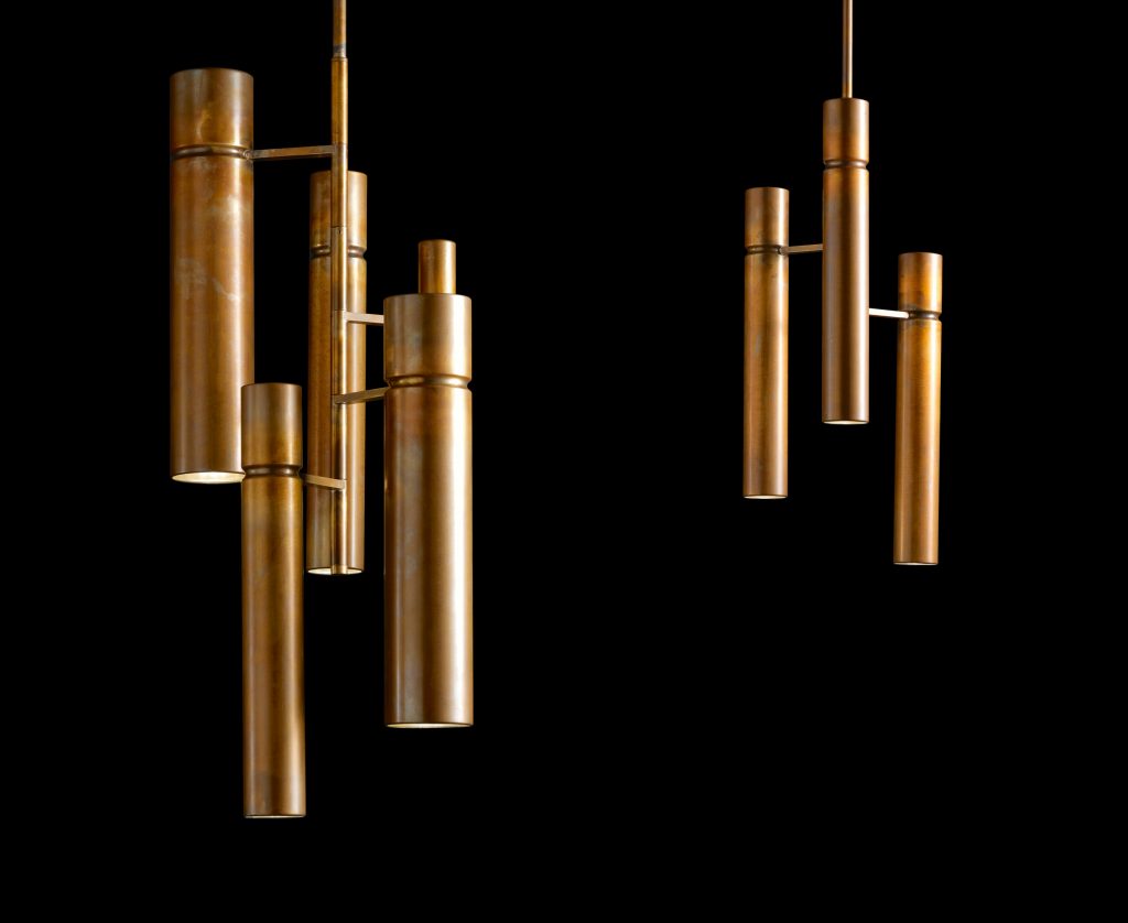 Two Tubular Ceiling Lights with a cylindrical shape in bronze joined with bronze-colored metal bars suspended with a rope on a black background.