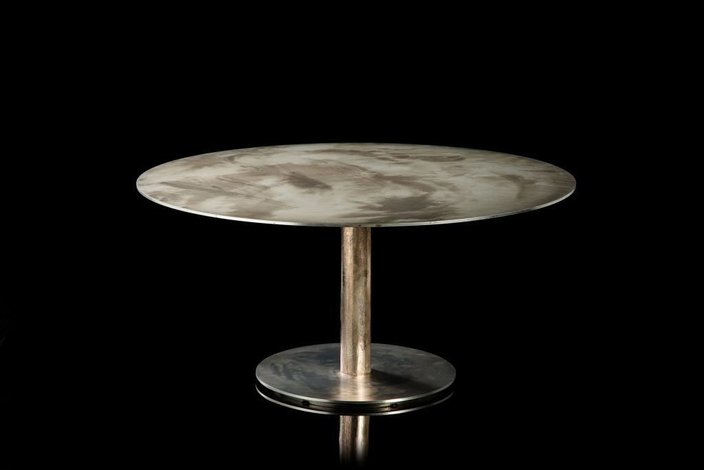 Round Twistable Coffe Table And Consolle. Structure support in silver, top in metal and central leg in burnished platino on a black background.