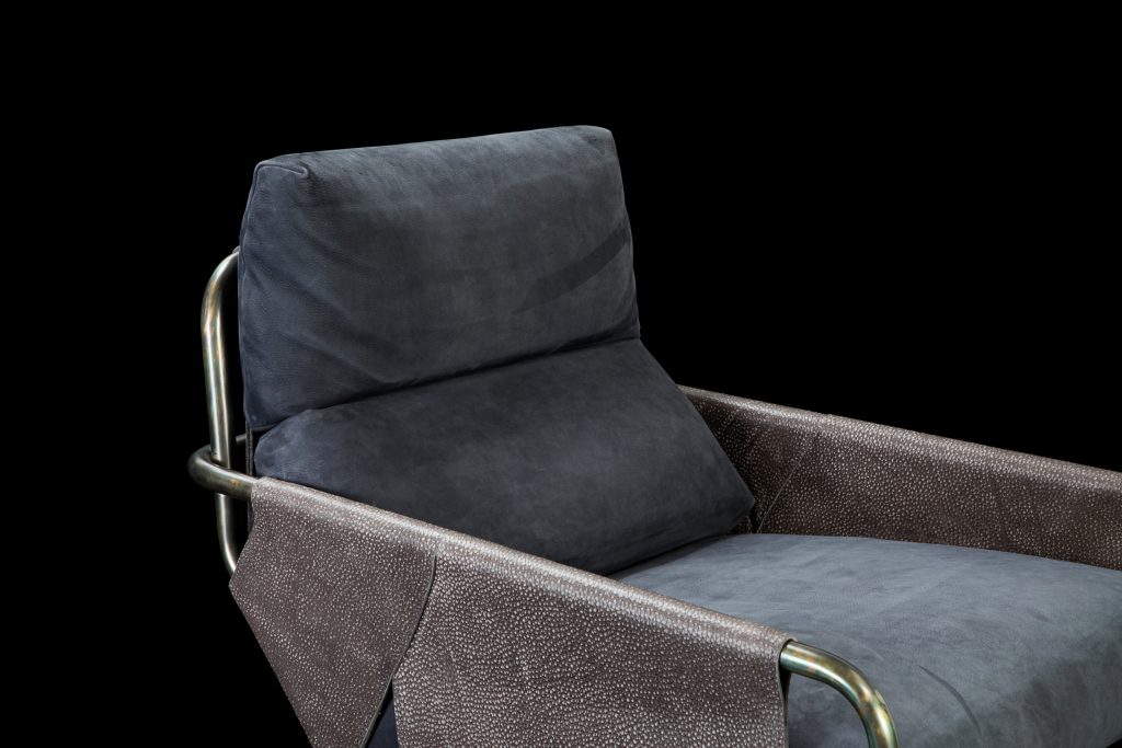 Voyage armchair, curved bronze steel structure with brown leather, gray leather cushion upholstery, central black steel leg on a black background.