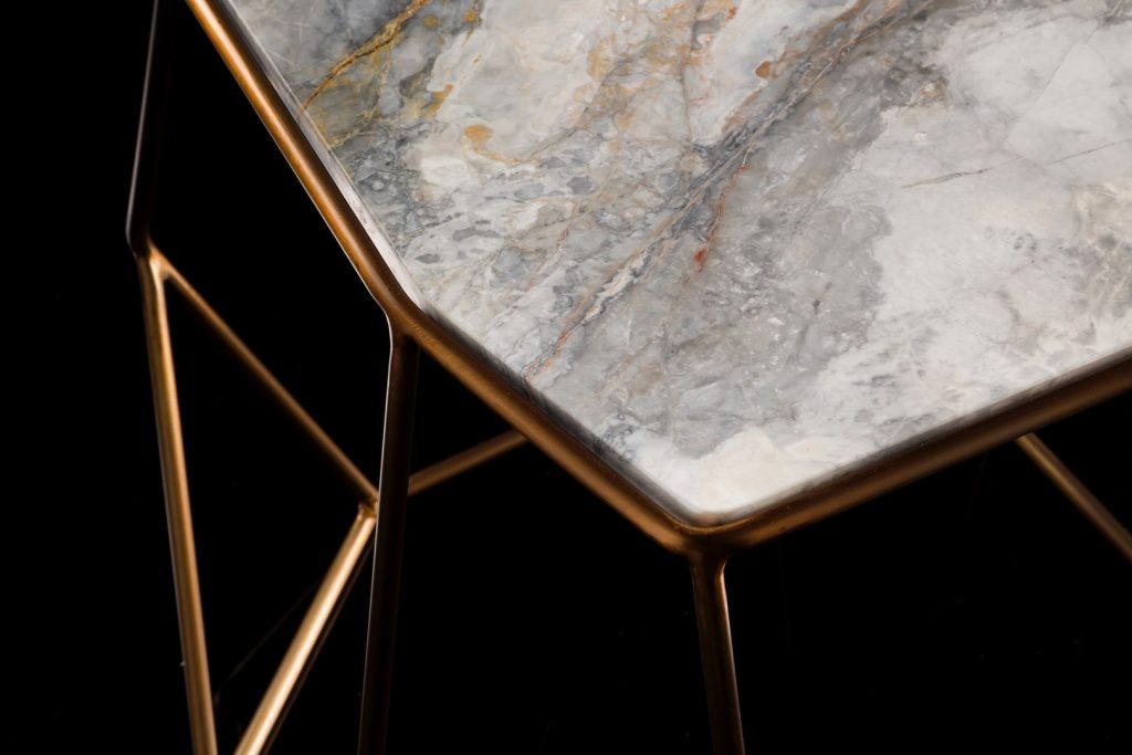 Closeup of W Table, structure in rod metal color bronze, diamond like shape. Top in white and gray marble on a black background.