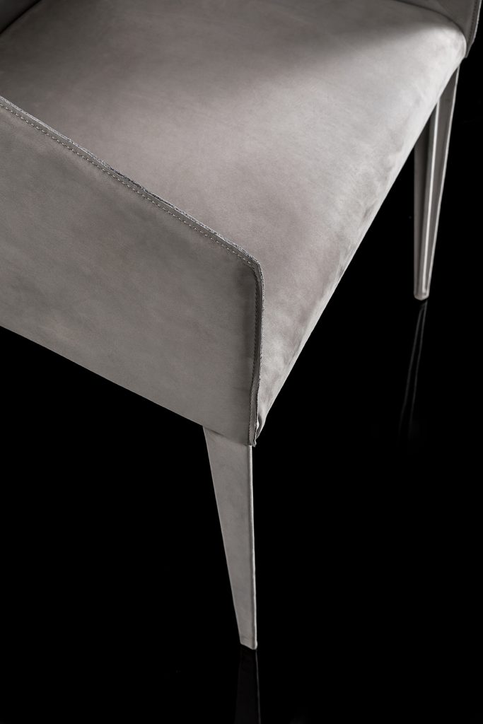 Closed up Zagg Chair, upholstered in gray fabric and four legs in silver steel on a black background.
