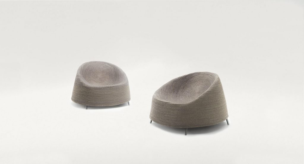 Two Afra Armchairs upholstered in beige cord sewn with a spiral-like pattern and four steel legs on a white background.