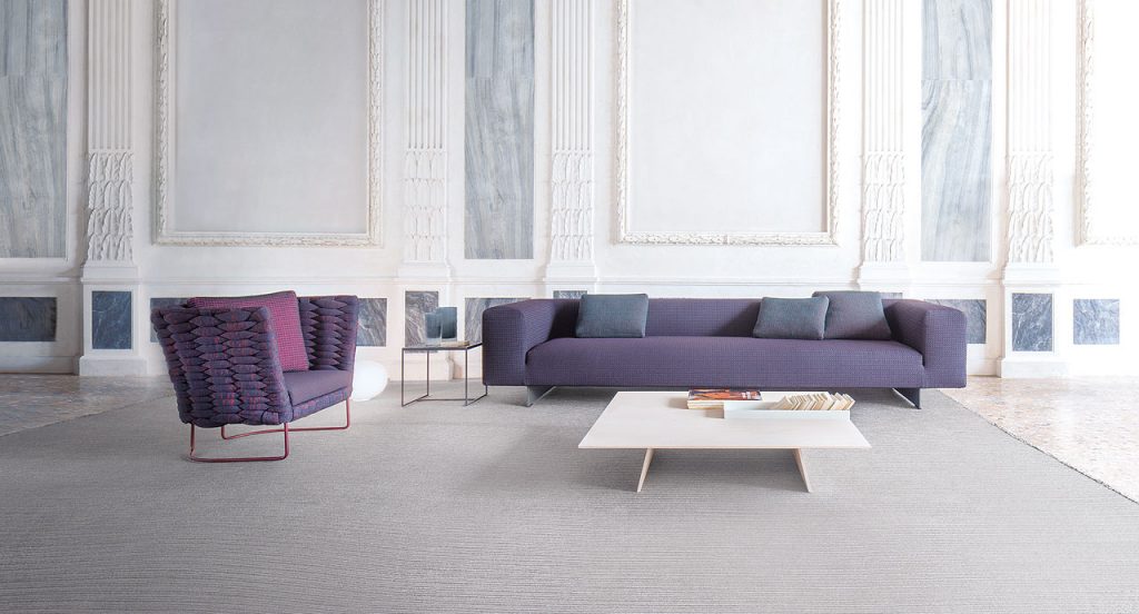 Atollo Next sofa, upholstery in purple fabric, two legs in steel in a living room.
