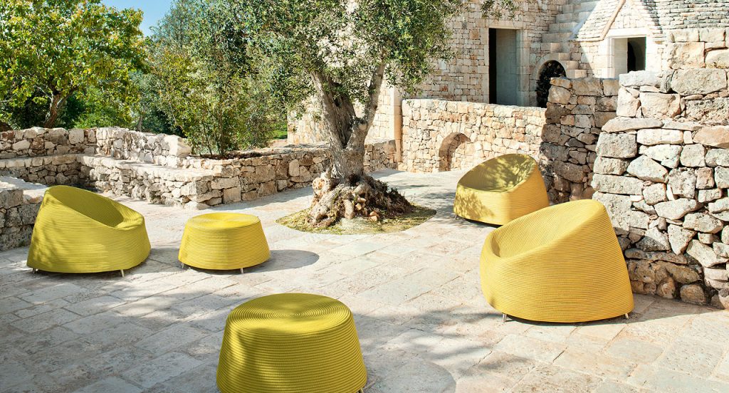 Three Afra Armchairs upholstered in yellow cord sewn with a spiral-like pattern and four steel legs on a terrace.
