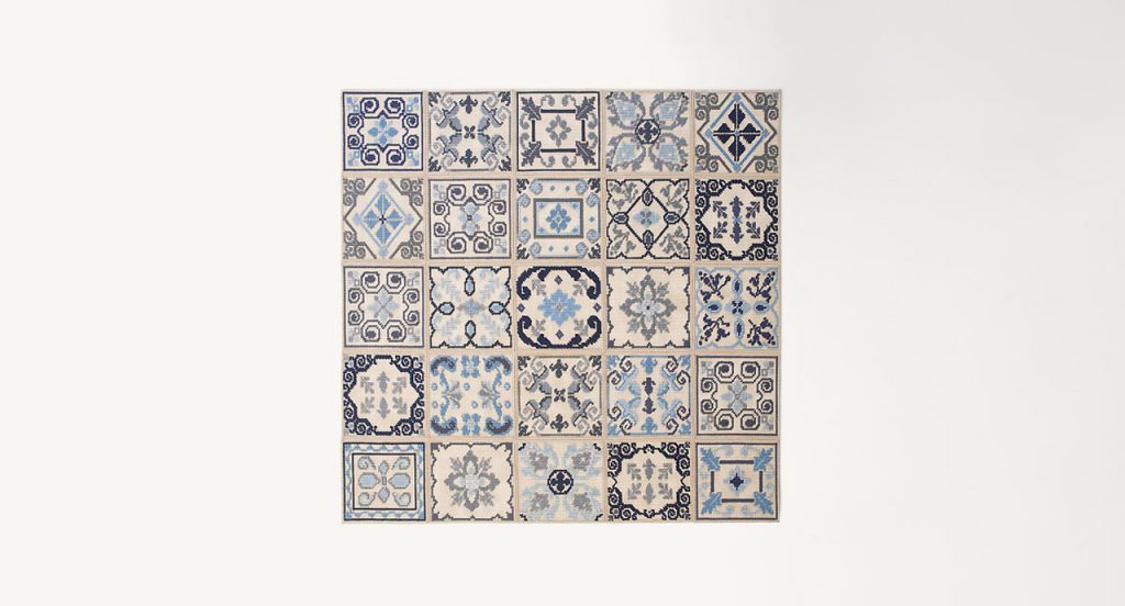 Donna Costanza rug embroidered with gray, blue, black and beige flat braids of abstract pattern on a white background.