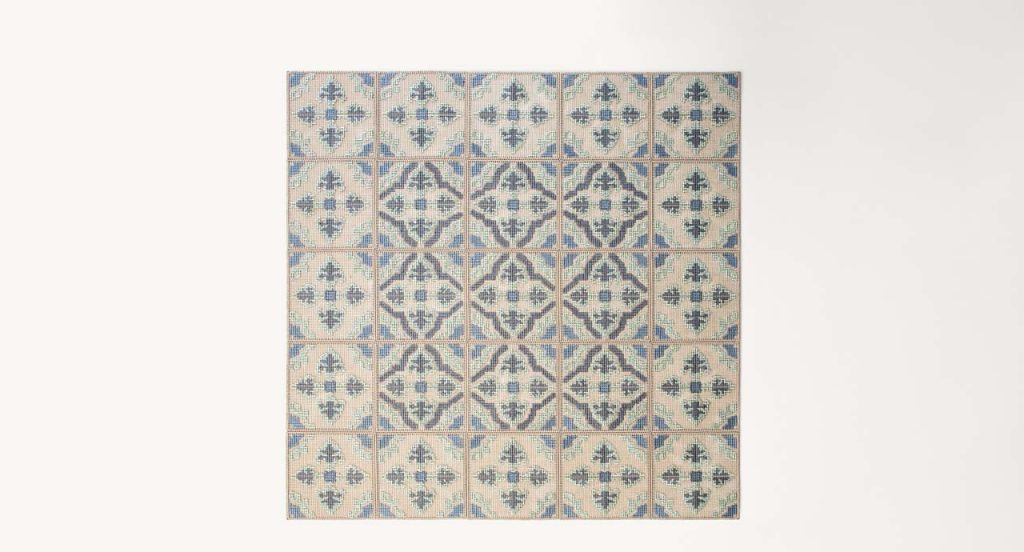 Donna Florio rug, embroidered with gray, blue, green and beige flat braids with a diamond like pattern on a white background.