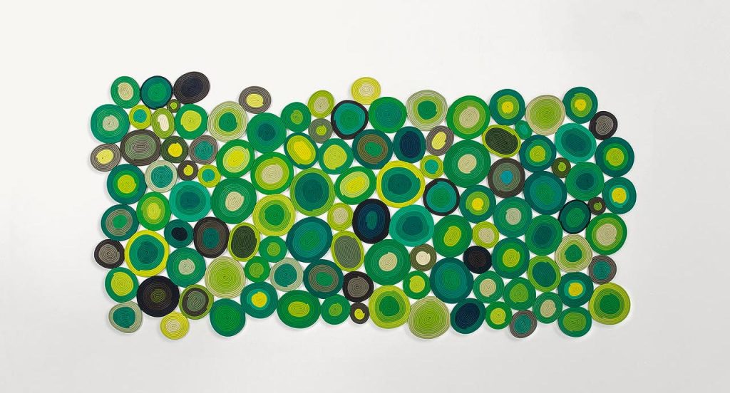 Ellissi rug made of yellow, green, blue, white and grey cords creating round and oval modules on a white background.