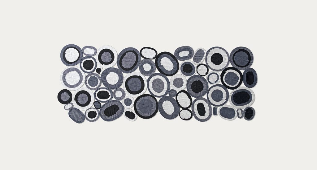 Ellissi rug made of white, grey and black cords creating round and oval modules on a white background.