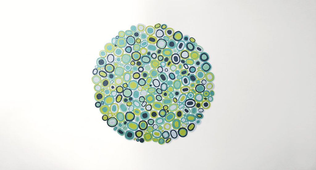 Ellissi rug made of yellow, green, blue, white and grey cords creating round and oval modules on a white background.