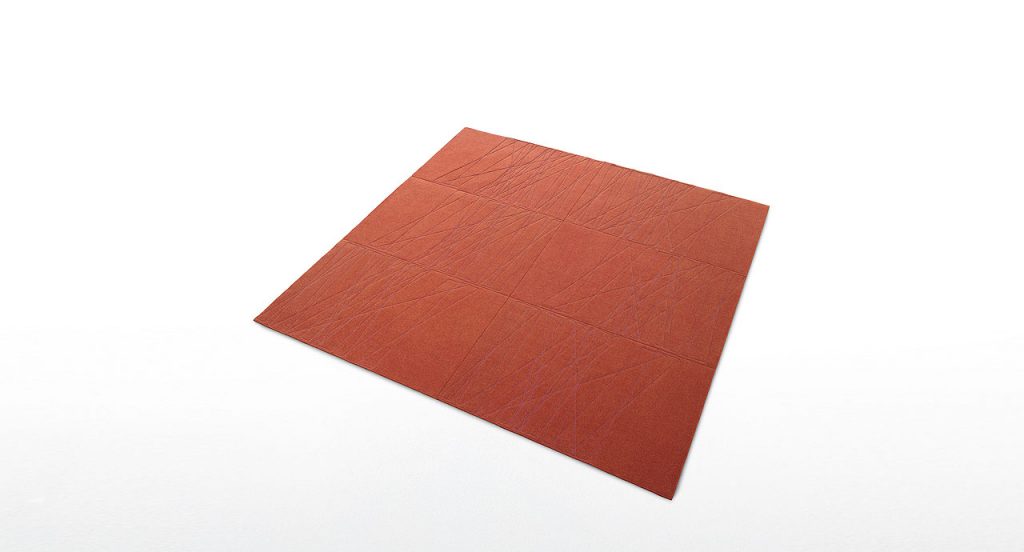 Flussi rug made of orange felt and embriodered in a rectangle on a white background.