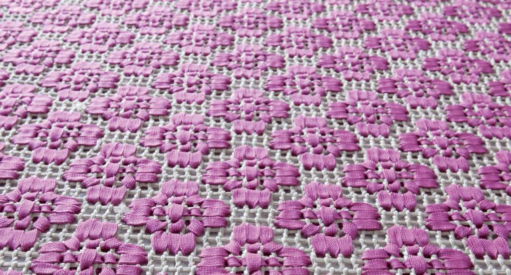 Giardino rug. The embroidery is made by white and purple flat braid.