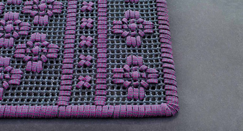 Giardino rug. The embroidery is made of grey and purple flat braid on a grey floor.