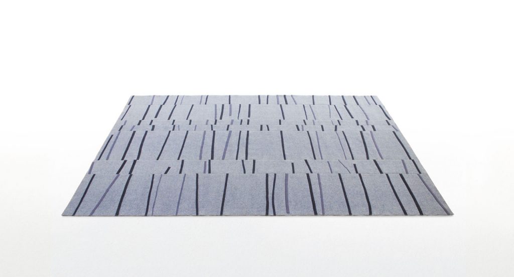 Graffito rug made of rectangles and strips in grey and black felt on a white background.